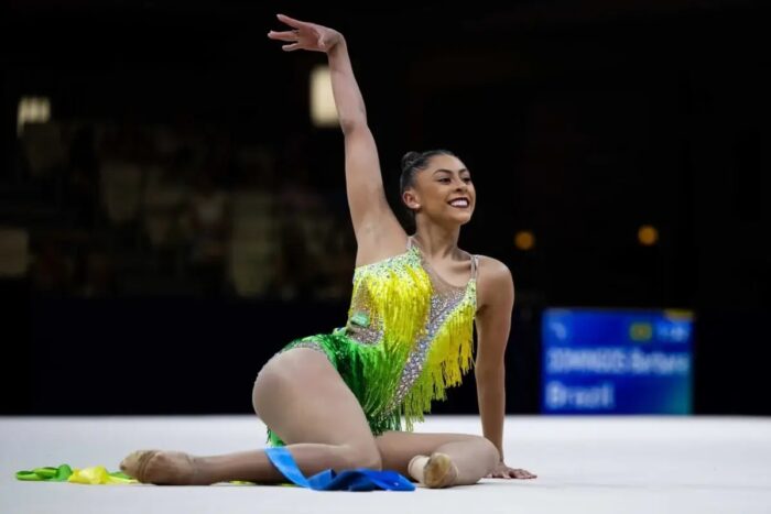 Ginasta Bárbara Domingos está sentada com collant nas cores do Brasil com o braço direito levantado