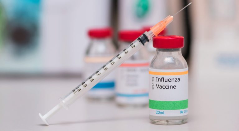 influenza vaccination concept with syringe in vaccine vial and other vials in background