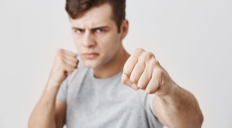 Angry agrressive young Caucasian male standing in defensive position, keeping fists clenched, having confident self-determined look, ready to defense himself and stands up for his rights