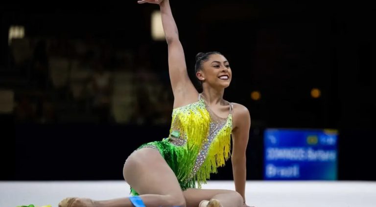 Ginasta Bárbara Domingos está sentada com collant nas cores do Brasil com o braço direito levantado