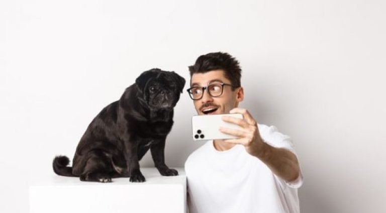 dono-de-cachorro-feliz-tirando-selfie-com-um-lindo-pug-preto-sorrindo-e-olhando-com-amor-para-o-cachorrinho-segurando-um-telefone-celular-branco_1258-32677-600x400