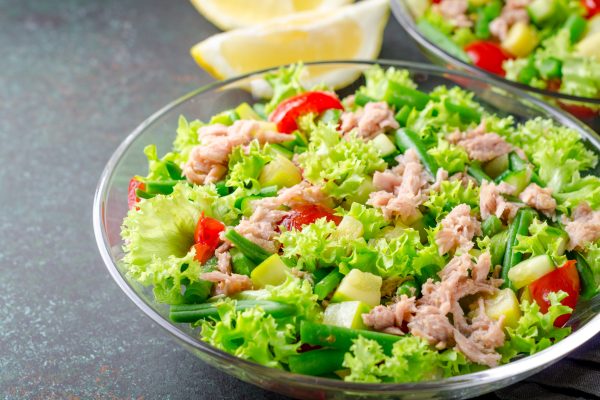 Fresh tuna salad with green beans and cherry tomatoes in a glass bowl on a dark stone table. High angle view, horizontal image, copy space
