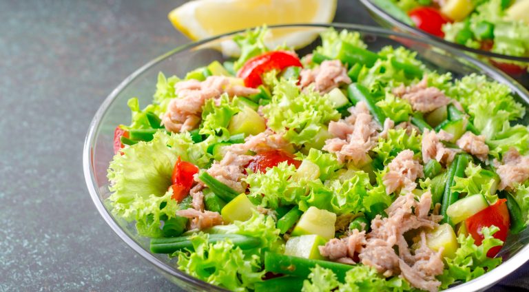 Fresh tuna salad with green beans and cherry tomatoes in a glass bowl on a dark stone table. High angle view, horizontal image, copy space
