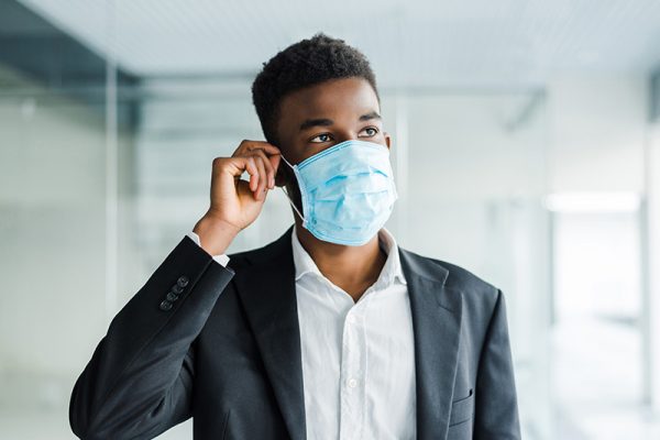 African young business man wearing a mouth protection to prevent getting sick at work in office