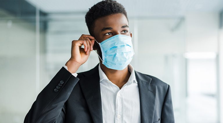 African young business man wearing a mouth protection to prevent getting sick at work in office