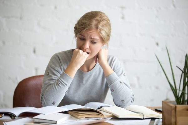 Portrait of a frustrated student girl sitting at the desk biting her fist. Education concept photo, lifestyle