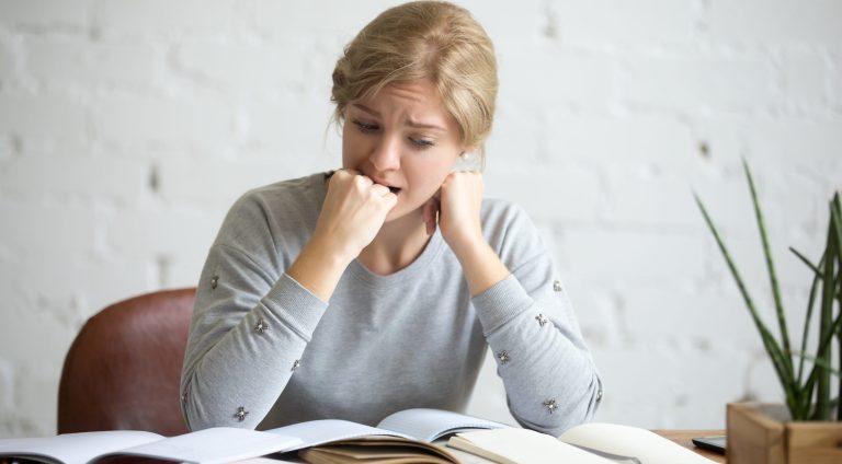 Portrait of a frustrated student girl sitting at the desk biting her fist. Education concept photo, lifestyle