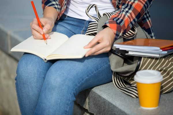 Student girl writing in an open notebook with a pencil. Back to school concept phot , closesup, horizontal