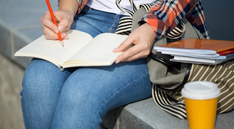 Student girl writing in an open notebook with a pencil. Back to school concept phot , closesup, horizontal